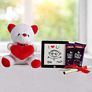 A hamper containing table top, dairy milk chocolates, cream teddy bear and a love message