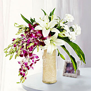 Glass vase arrangement of 6 purple orchids, 3 white asiatic lilies, 6 white carnations with draceane leaves and vase filler