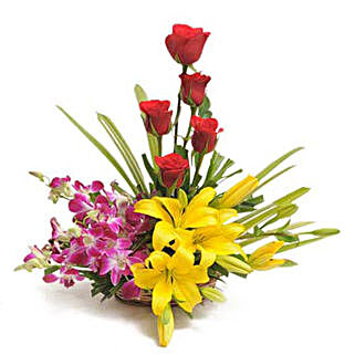 Cane basket arrangement of 5 red roses, 4 purple orchids, 2 yellow asiatic lilies and draceane leaves