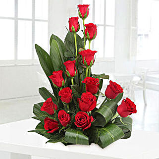 Cane basket arrangement of 15 red roses, draceane leaves and seasonal filler